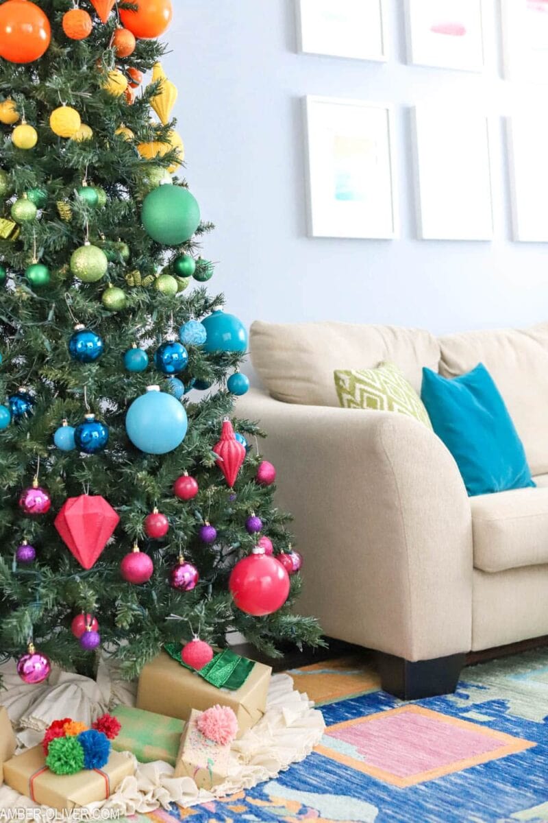 Christmas tree decorated in rainbow colored ornaments with presents underneath.