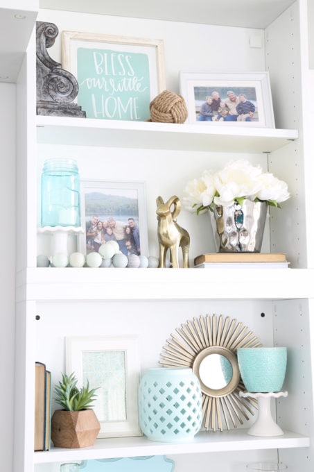 It can be a challenge to know how to decorate shelves, but this foolproof formula will teach you how to style shelves beautifully in no time! | #shelfie #shelfstyling #styledshelves #bookshelfstyling #livingroom #livingroomdecor #summerdecor #vignette Decorated Shelves with Aqua, White, and Neutral Coastal Decor