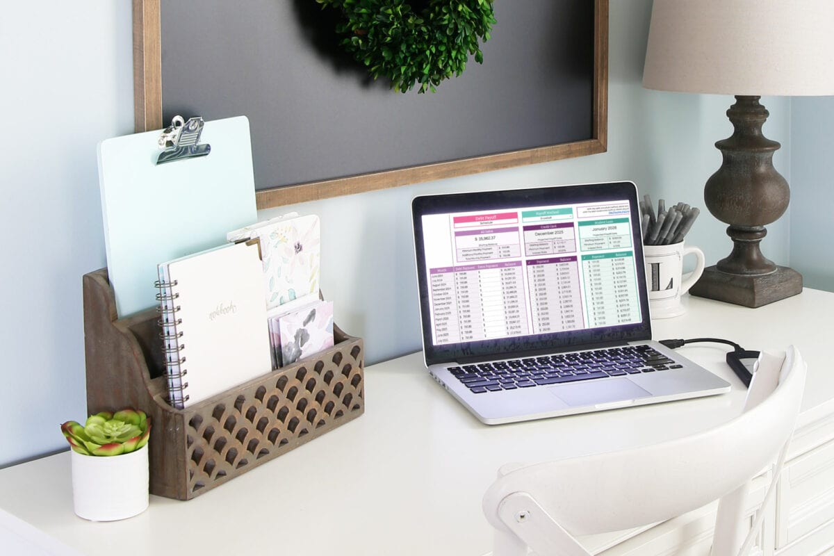 Laptop computer sitting on a white desk in an organized home office, displaying a Debt Snowball Spreadsheet to help pay down debt