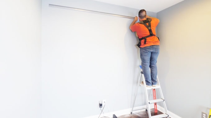 Man on a ladder installing an Elfa shelving unit from The Container Store