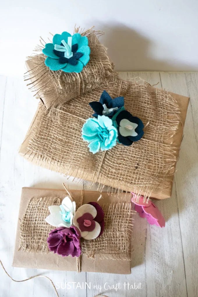Three packages wrapped in brown paper and burlap with felt flowers on top of a beautifully wrapped gift.