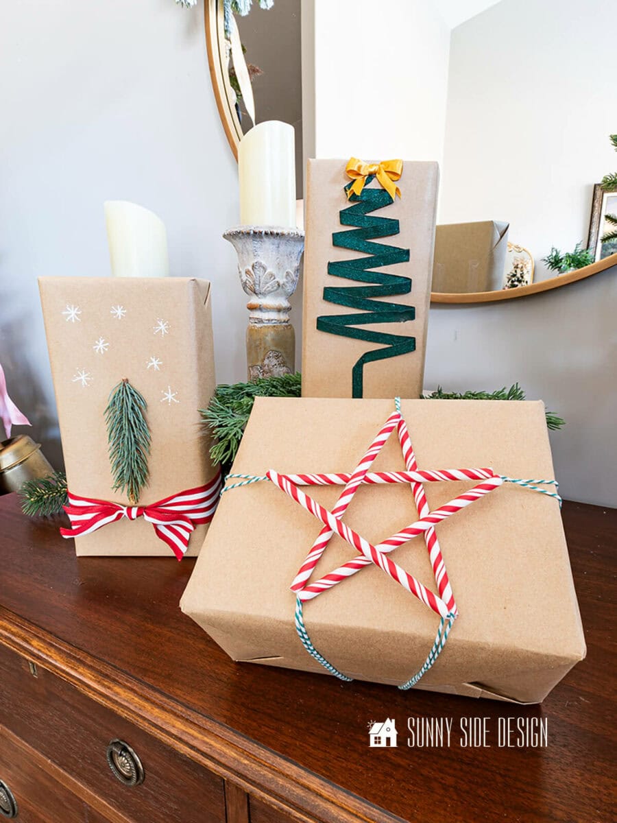 Three wrapped presents in brown construction paper with cute tree and star embelishments sitting on a dresser in front of a mirror.