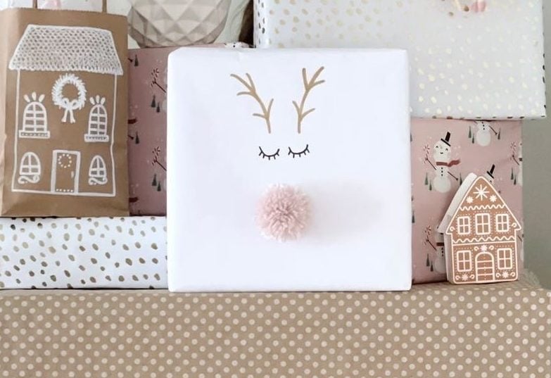 A white package gift wrapped with a hand-drawn reindeer on top of polka dot brown paper in front of other gifts