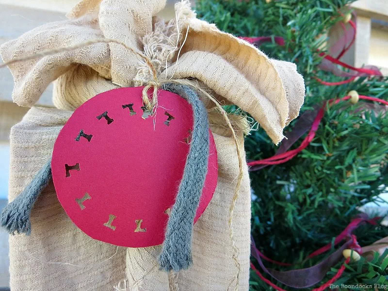 A beautifully wrapped gift in vintage wrapping with a red circle tag sitting in front of a Christmas tree.