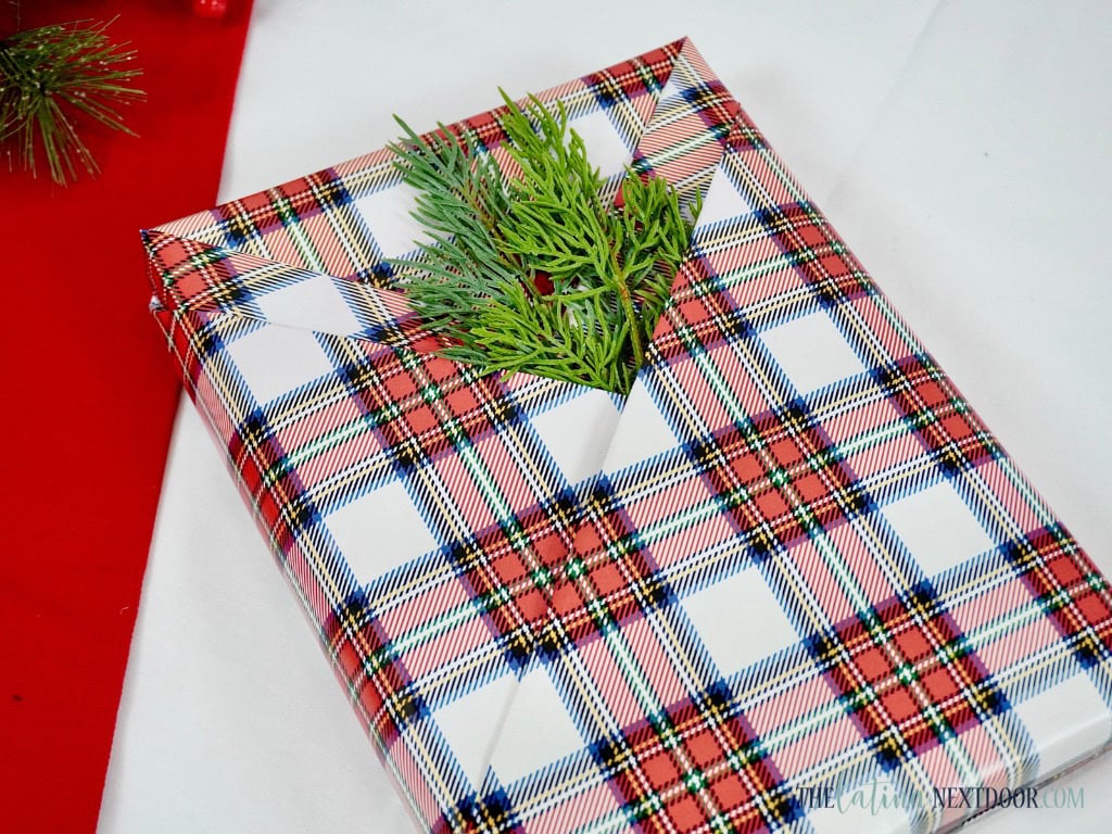 A beautifully wrapped gift in red plaid paper with a sprig of greenery tucked into the fold, offering a unique gift wrapping idea for a festive look.